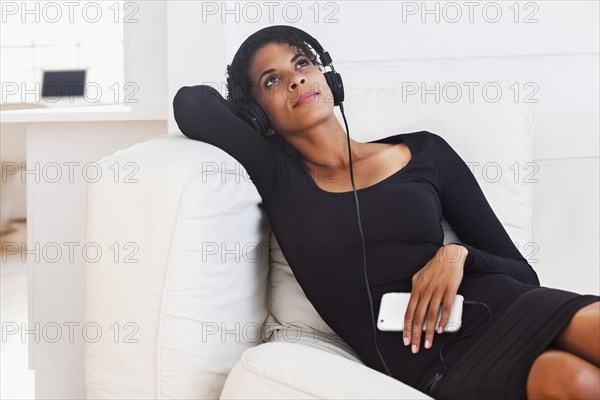 Mixed Race woman on sofa listening to cell phone with headphones