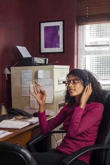 Mixed Race businesswoman listening to headphones in office