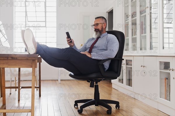 Caucasian man with feet up texting on cell phone