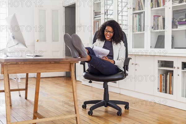 Mixed Race woman with feet up writing on notepad