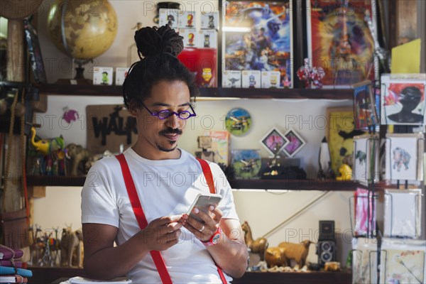 Serious mixed race man wearing suspenders texting on cell phone