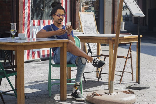 Mixed race man with prosthetic leg texting on cell phone at sidewalk cafe