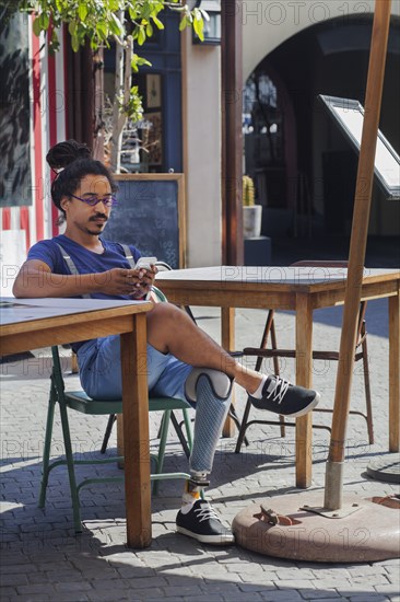 Mixed race man with prosthetic leg texting on cell phone at sidewalk cafe