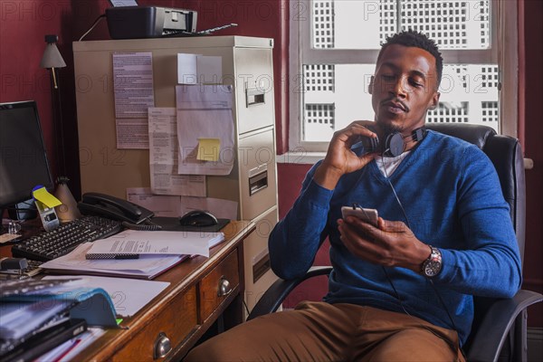 Black man reading cell phone and holding headphones