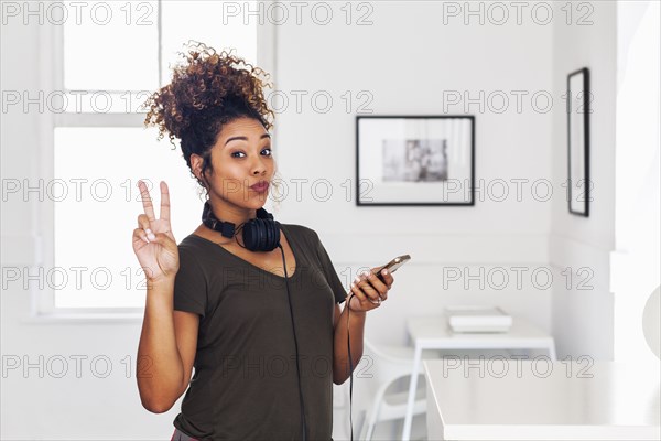 Mixed race woman holding cell phone gesturing peace