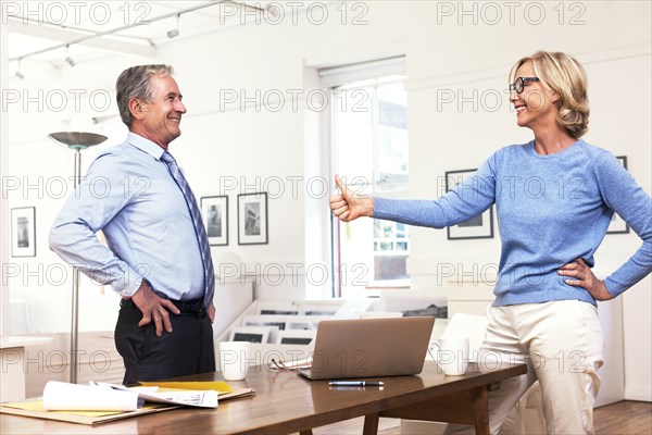 Caucasian businesswoman gesturing thumbs-up to businessman