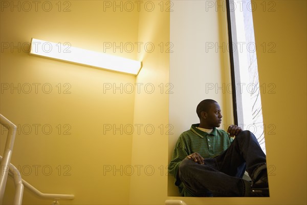 African teenager sitting in window sill