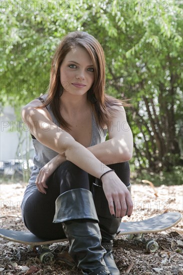 Smiling Caucasian teenage girl sitting on skateboard