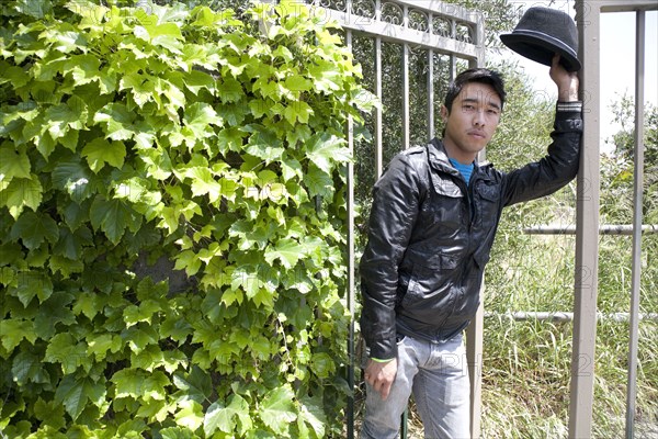 Mixed race teenage boy leaning against gate and looking serious