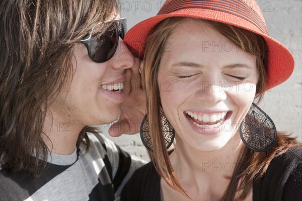 Close up of teenage boy whispering in smiling girl's ear