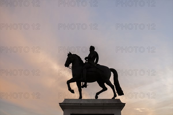 Silhouette of horse and rider statue under sunset sky