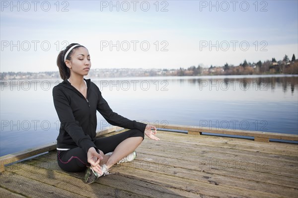 Mixed race woman practicing yoga on pier