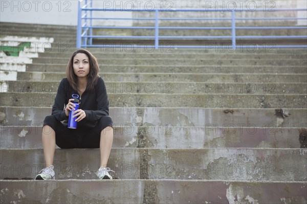 Mixed race woman with water bottle sitting in stadium