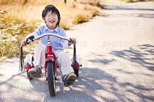 Chinese boy riding tricycle on sidewalk