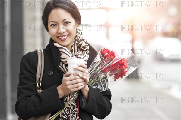 Mixed race woman holding coffee and bouquet of flowers