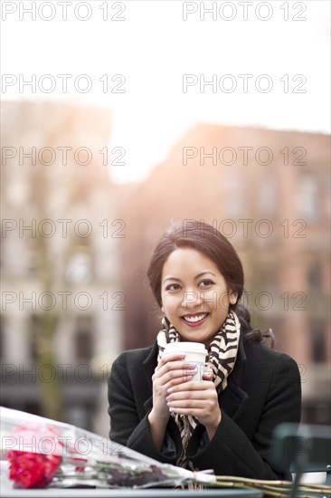 Mixed race woman holding coffee with bouquet of flowers