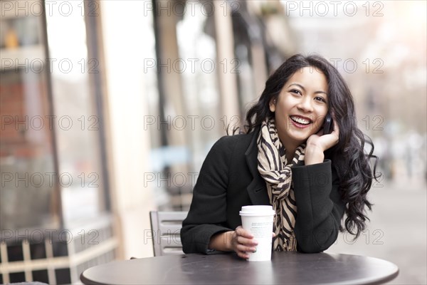 Mixed race woman talking on cell phone and drinking coffee
