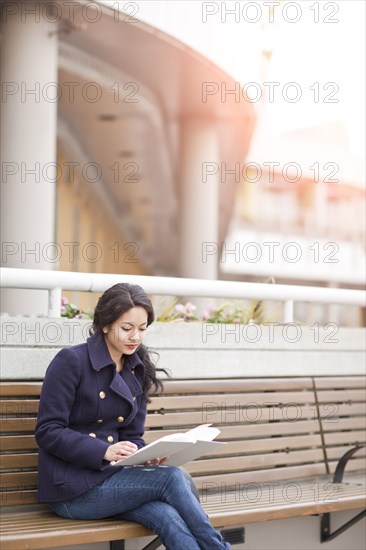 Mixed race woman sitting on bench reading
