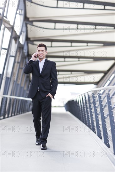 Mixed race businessman walking and talking on cell phone