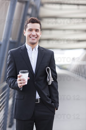 Mixed race businessman carrying coffee and newspaper