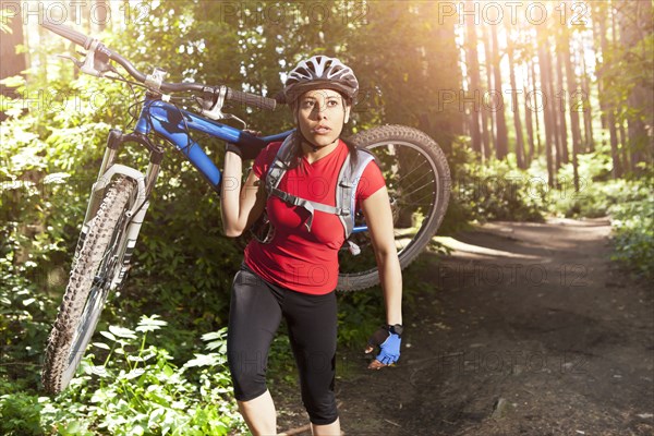 Hispanic woman carrying mountain bike in forest