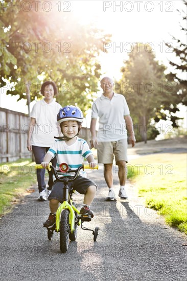 Chinese grandparents watching grandson riding bicycle