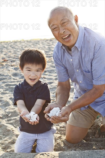Chinese grandfather and grandson gathering shells on beach