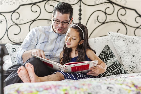 Father reading to daughter on bed