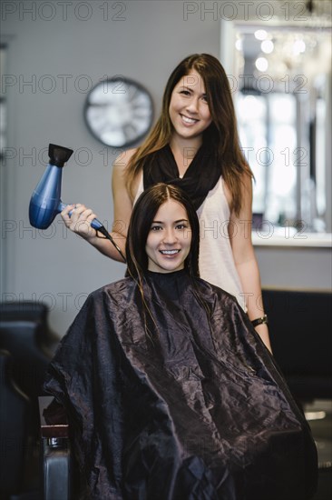 Stylist blow drying client's hair in salon