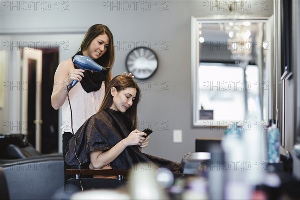 Stylist blow drying client's hair in salon