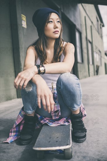 Korean woman sitting on skateboard on city street