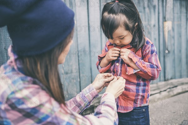 Korean mother helping daughter button her shirt