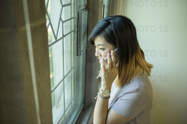 Chinese woman standing near window talking on cell phone