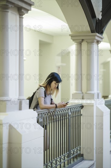 Chinese woman leaning on railing texting on cell phone