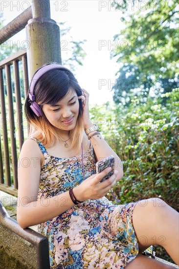 Chinese woman sitting outdoors listening to cell phone with headphones