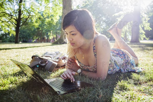 Chinese woman laying on grass using laptop