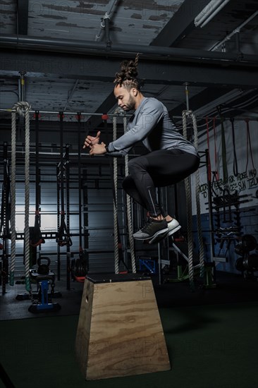 Mixed Race man jumping on wooden platform in gymnasium
