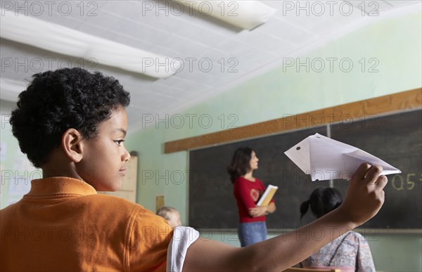 Mixed Race boy throwing paper airplane in class