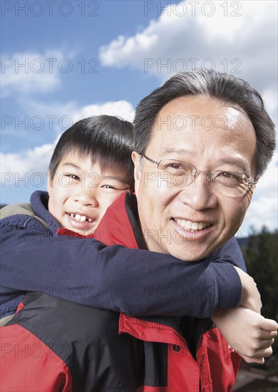 Asian father giving son piggyback ride outdoors