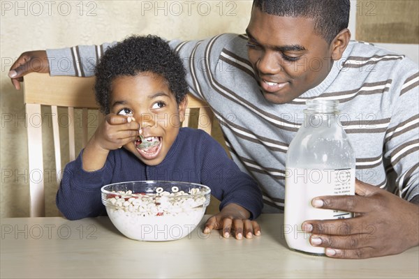 Young African American boy eating cereal with father