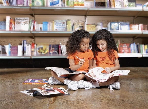 Two young sisters reading books in library