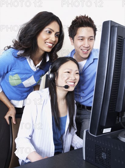 Young Asian female computer service technician with coworkers looking over her shoulder