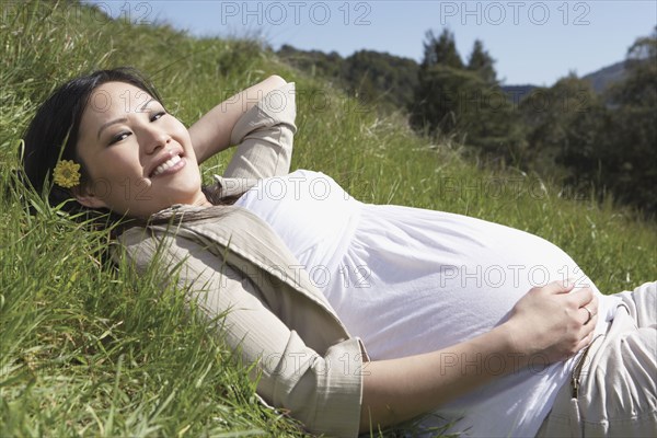 Pregnant Asian woman laying in the grass