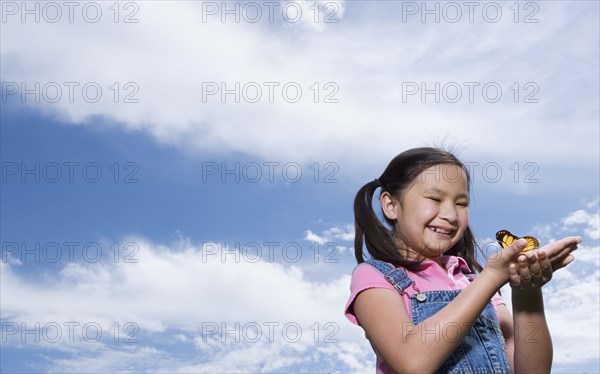 Young Asian girl holding butterfly outdoors