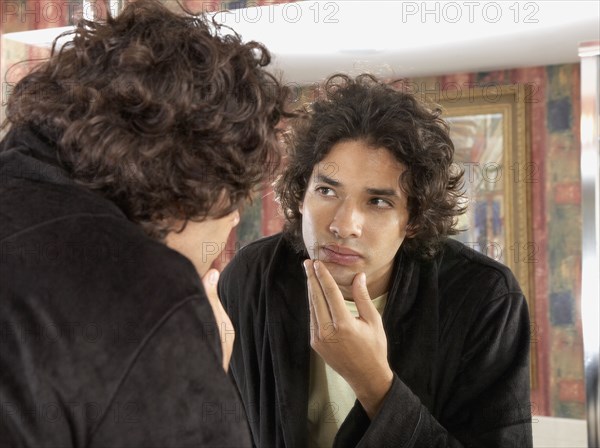 Hispanic man looking in bathroom mirror