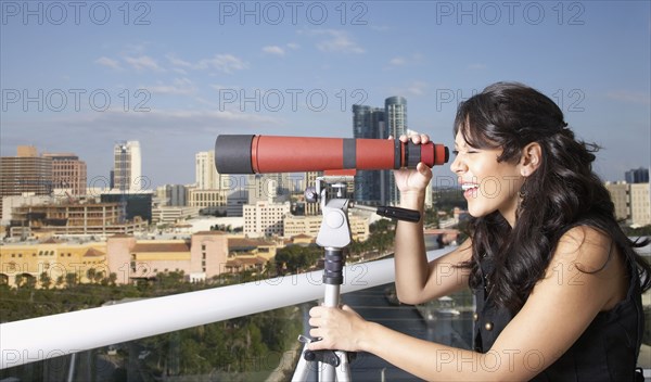 Hispanic woman looking through telescope on balcony