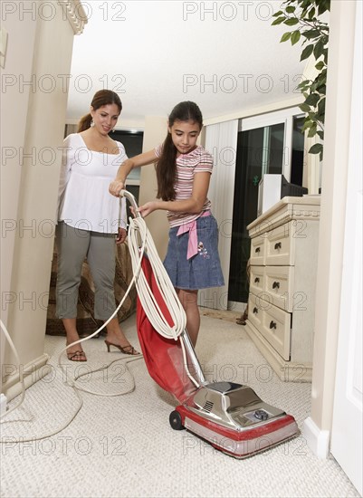 Hispanic mother watching daughter vacuum