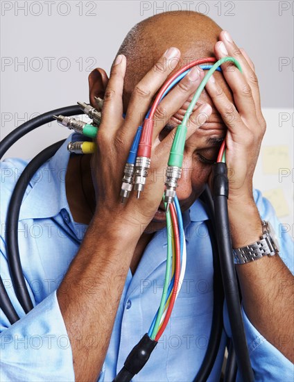 African businessman holding computer cables with head in hands