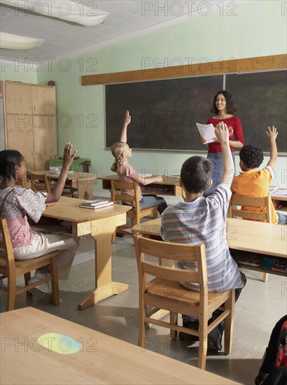 Multi-ethnic students raising hands in class