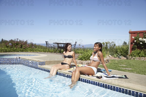 Multi-ethnic women with feet in swimming pool